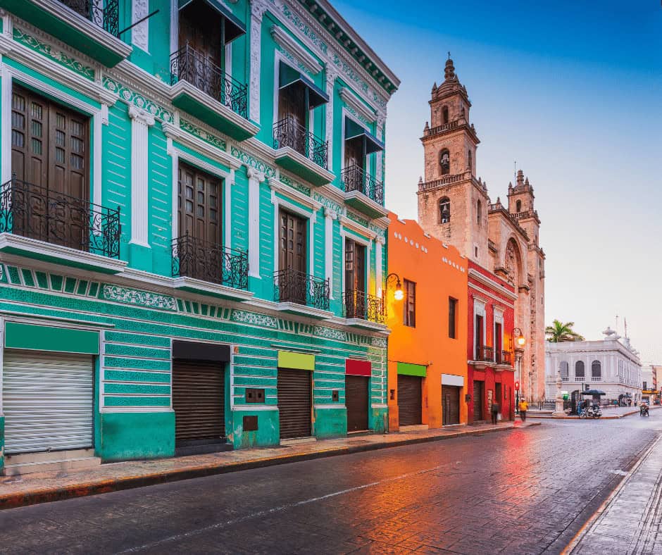 Colorful colonial buildings in Oaxaca, Mexico, with a church tower in the background at dusk.