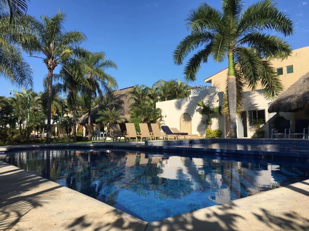 Resort pool area with palm trees, lounge chairs, and a thatched roof building in Puerto Vallarta, Mexico.